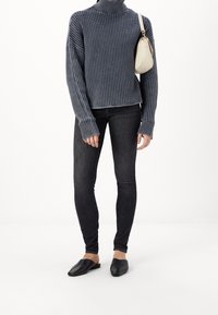 Un pull à col roulé côtelé bleu foncé, un jean skinny noir et des mules plates noires, avec un petit sac à main clair.