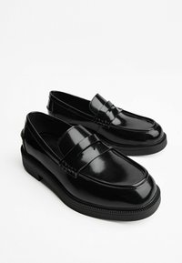 Pantofi loafers din piele patent neagră cu o finisare netedă, având un detaliu cu curea frontală, talpă texturată și un toc jos, solid.