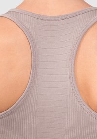 Top sin mangas acanalado en suave topo, con amplios agujeros para los brazos y un panel trasero texturizado con líneas horizontales para mayor transpirabilidad.