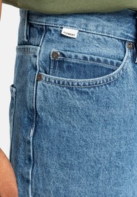 Helle blaue Jeansshorts mit verwaschener Textur, ausgestattet mit silbernen Beschlägen, Taschen und einem "Element"-Label am Bund.