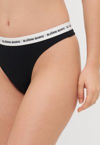 Černé bikini kalhotky s bílým elastickým pasem, na kterém je text "BJÖRN BORG." Tkanina vypadá hladce a má přiléhavý střih.
