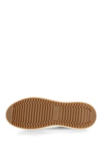 Soletta di scarpa in gomma color beige con un motivo testurizzato e a righe. Presenta un bordo bianco e un'etichetta con logo. Design piatto per comfort e aderenza.