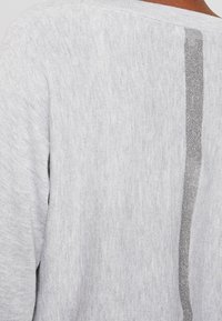 Maglione a maglia grigio chiaro con una striscia verticale grigia metallica sul retro. Tessuto morbido, scollatura a girocollo e maniche lunghe.