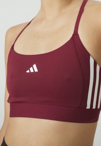 Mörkröd sportbh med tunna axelband, med en vit logotyp på framsidan och texturerade, ribbade detaljer på sidorna och nederkanten.