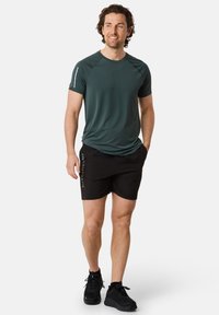 Sport t-shirt i mörkgrön, kort ärm, med ett reflekterande detaljer. Svarta shorts med sidologotyp. Svarta träningssneakers.