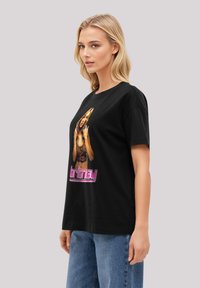 Black cotton t-shirt featuring a central graphic of a woman, with pink text reading "britney." The shirt has short sleeves and a relaxed fit.