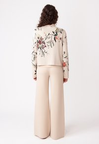 Beige gebreide trui met bloemembroidered in roze, rood en groen; gecombineerd met beige gebreide broek met hoge taille en wijde pijpen.