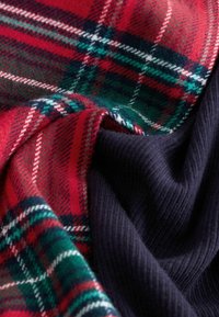 Red and green plaid fabric with white lines, paired with a dark navy ribbed texture. Soft, warm, and layered with visible folds.
