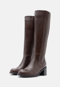 Καφέ δερμάτινες μπότες μέχρι το γόνατο με λείο φινίρισμα, τετράγωνη σόλα και κάθετες ραφές στις πλευρές.