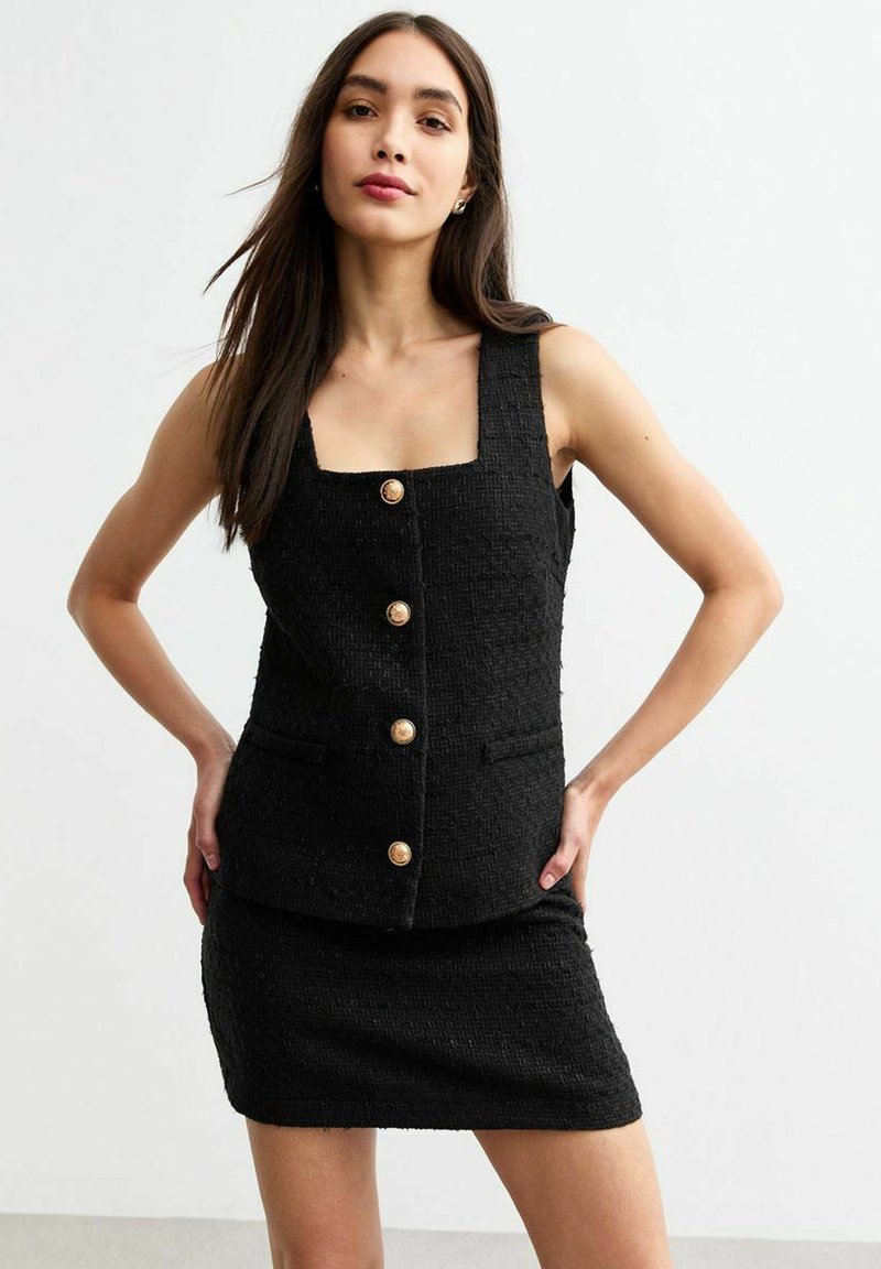 Zwart tweedelig outfit met een getextureerd mouwloos top met vierkante halslijn en gouden knopen, gecombineerd met een aansluitende mini-jurk.