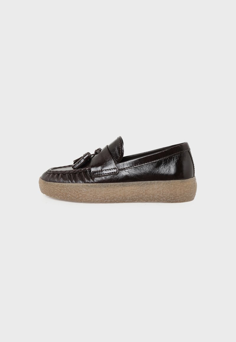Mocassin en cuir noir avec détail à pampille et semelle en caoutchouc beige texturée, présenté de côté sur un fond clair uni.