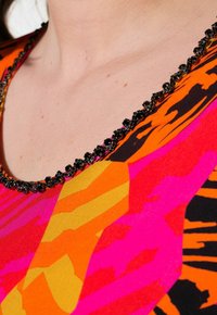 Mehrfarbige gemusterte Bluse mit leuchtenden Orange-, Pink- und Gelbtönen. Schwarze Perlenverzierung am Ausschnitt sorgt für Detailreichtum. Weicher Stoff.