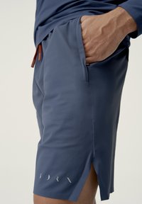 Mørkeblå atletikshorts med en glat overflade, der har en sidelomme, slids på kanten og subtile reflekterende detaljer nær kanten.