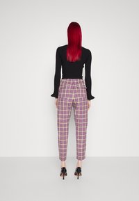 Haut à manches longues noir à côtes associé à un pantalon à carreaux taille haute dans des teintes de violet, jaune et beige, avec des jambes fuselées et des escarpins noirs élégants.