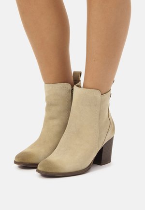 Stivaletti alla caviglia in suede beige con punta appuntita e tacco a blocco di 7 cm. Presentano una cerniera laterale e un tassello per un facile indossamento.