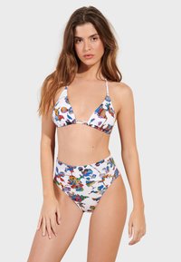 Bikini set s barevným zvířecím vzorem na bílém pozadí. Vrchní část má trojúhelníkový design s nastavitelnými ramínky a spodní část je vysoká v pase.