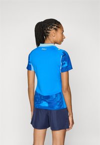 Top corto blu a maniche corte con parte superiore unita e parte inferiore a fantasia, dotato di colletto, dettagli gialli e un paio di pantaloni corti blu navy.