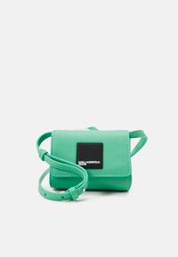 Borsa a tracolla verde in ecopelle con flap, tracolla regolabile e patch logo quadrato. Texture liscia e forma rettangolare compatta.