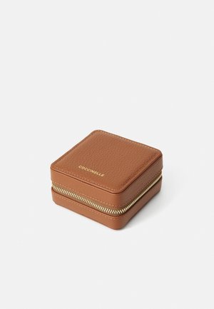 Étui à bijoux carrée en cuir brun avec surface texturée, fermeture éclair dorée et logo en relief sur le dessus. Design compact pour un rangement facile.