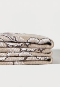 Tres piezas de tela beige dobladas con patrones florales en blanco y marrón apiladas sobre una superficie blanca y lisa.