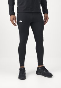 Czarne legginsy sportowe o dopasowanym kroju, z białym logo i gładką teksturą. W połączeniu z czarnymi butami sportowymi.
