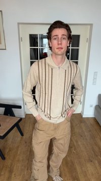 Νέος άνδρας που στέκεται μέσα σε κλειστό χώρο με τα χέρια στις τσέπες, φοράει μπεζ μακρυμάνικο πουκάμισο με κάθετες καφέ ρίγες και χακί παντελόνι.