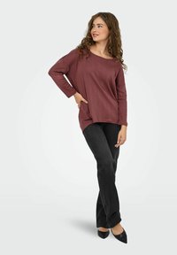 Top a maniche lunghe bordeaux con un motivo testurizzato, abbinato a jeans neri a gamba dritta e ballerine nere a punta.