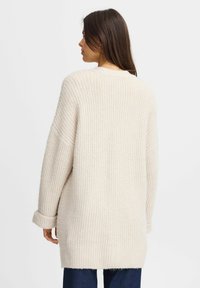 Cardigan oversize beige in maglia con texture a coste, maniche lunghe e polsini arrotolati. Il retro presenta un design semplice e pulito.