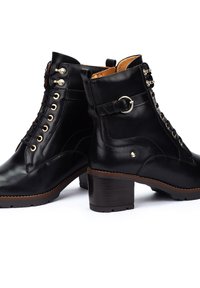 Botas de tobillo de cuero negro con punta redondeada, accesorios en tono dorado y un detalle de tira texturizada; cuentan con un tacón ancho y un diseño con cordones.