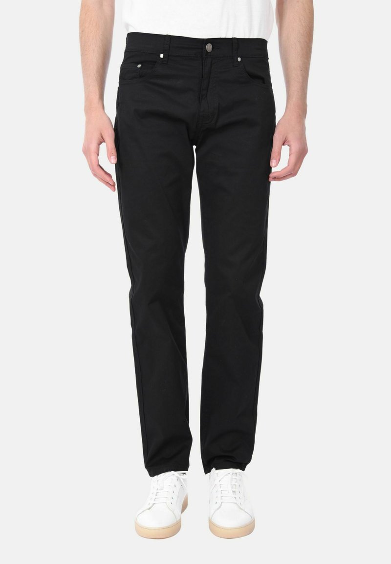 Pantaloni di cotone neri con vestibilità regolare, cinque tasche e chiusura con zip. Presentano dettagli metallici argentati e una texture sottile. Indossati con sneakers bianche.