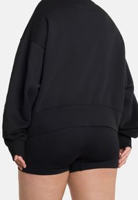 Černá oversized mikina s kleslými rameny, spárovaná s texturovanými černými žebrovanými šortkami. Oba kusy mají volný střih a minimalistický design.