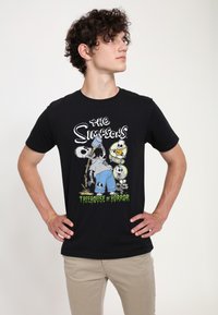 T-shirt en coton noir avec un graphisme "Les Simpson" comprenant des designs de squelette et le texte "Treehouse of Horror" en vert. Manches courtes et col ras du cou.