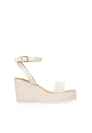 Sandalias de cuña en tejido trenzado crema con correa en el tobillo y hebilla, que muestran un diseño texturizado y trenzado y una base de tacón de madera.