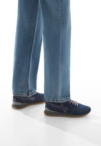 Scarpe sportive blu navy con parte superiore in suede testurizzato e mesh, dettagli grigi e chiusura con lacci; abbinate a jeans azzurri a gamba dritta.