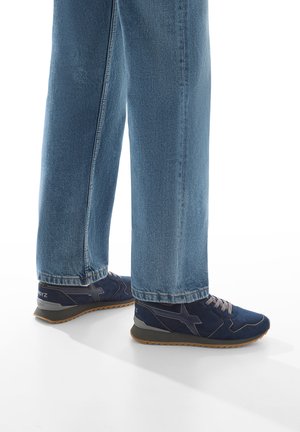 Scarpe sportive blu navy con parte superiore in suede testurizzato e mesh, dettagli grigi e chiusura con lacci; abbinate a jeans azzurri a gamba dritta.