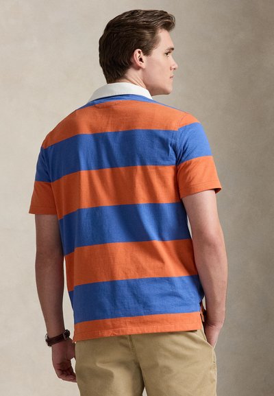 Πόλο μπλούζα με κοντά μανίκια που διαθέτει οριζόντιες πορτοκαλί και μπλε ρίγες, με λευκό γιακά σε αντίθεση. Υλικό από βαμβάκι, άνετη εφαρμογή.