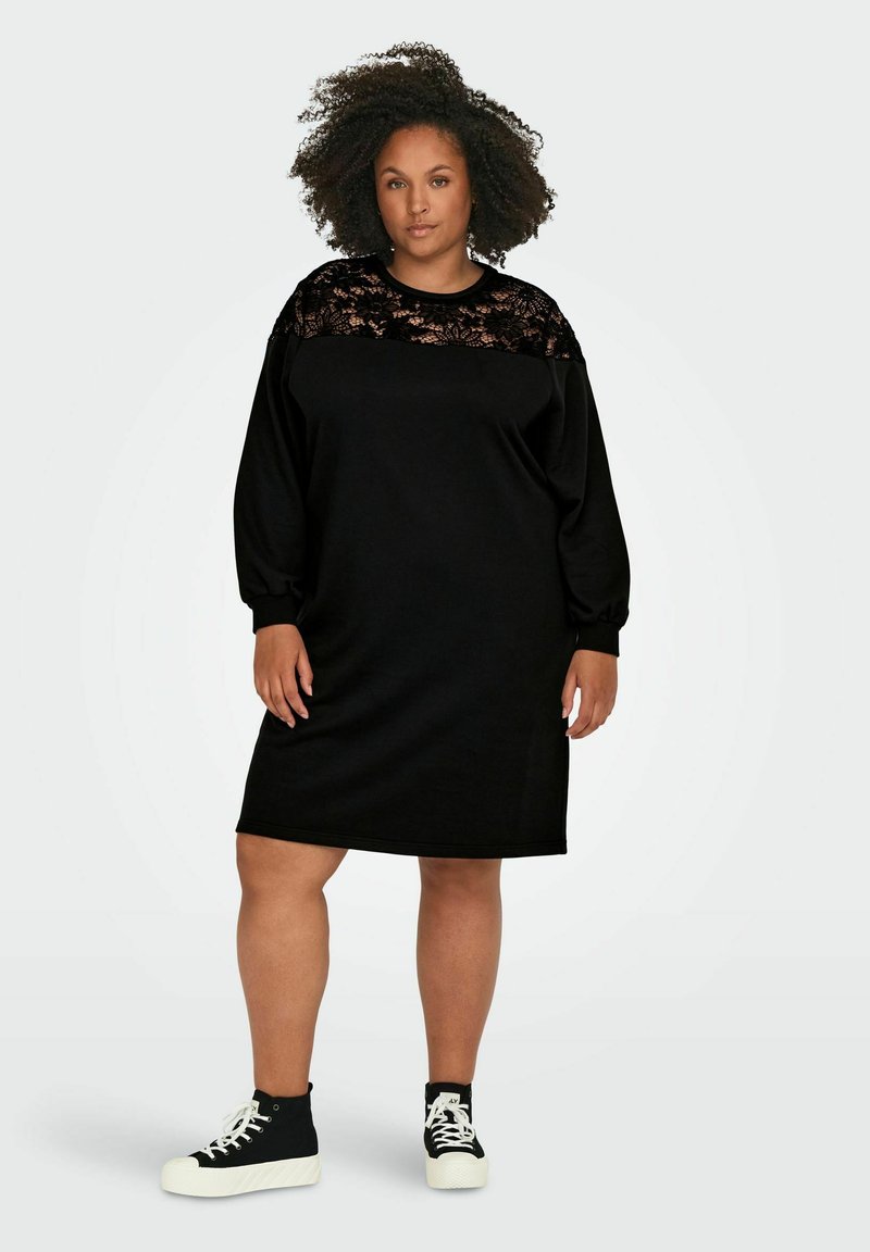 Vestido sudadera negro con panel superior de encaje, mangas largas y un corte relajado. Combinado con zapatillas negras de caña alta.