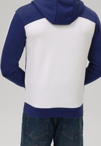 Felpa con cappuccio blu navy e bianca con sezione superiore della spalla a contrasto, texture liscia e orlo rifinito, abbinata a jeans blu.