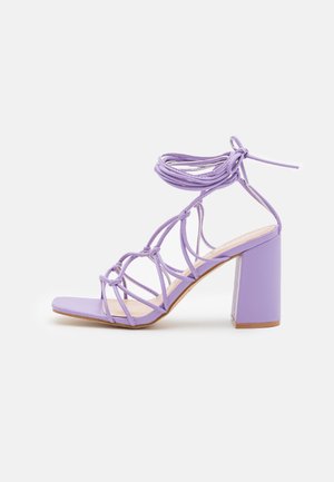 Lavendel højhælet sandal med firkantet tå, blokhæl og flere tynde stropper, der vikles og bindes omkring anklen.