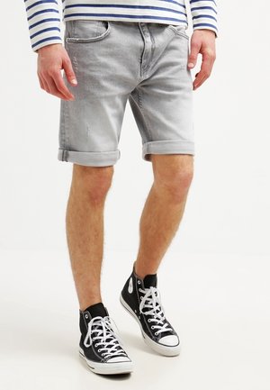 Jasnoszare szorty dżinsowe z podwiniętymi mankietami, charakteryzujące się przetarciami. W połączeniu z czarnymi wysokimi trampkami z białymi sznurówkami.