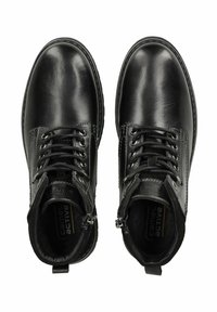 Botas de tacón de piel negra con punta redonda. Cuentan con cordones y una cremallera lateral, con un detalle de costura a lo largo de las suelas.