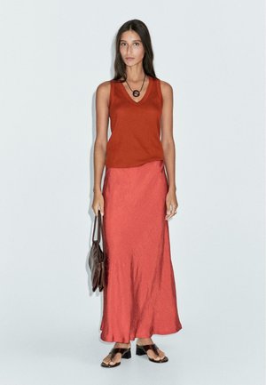 Canotta ruggine con scollo a V, abbinata a una gonna lunga arancione. L'outfit è completato da sandali piatti neri e una borsa marrone scuro.