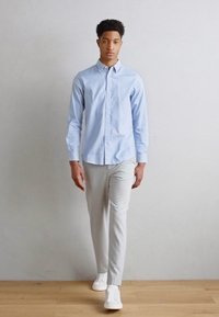 Hellblaues Hemd mit Knopfleiste, lange Ärmel, kombiniert mit hellgrauen Hosen und weißen Sneakers. Glattes Material und strukturierte Passform. Minimalistisches Design.