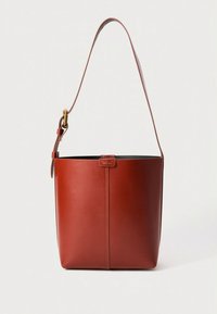 Punainen nahkainen säilytyskassi, jossa on sileä pinta, yksi olkahihna ja hienovarainen logokoriste edessä. Yksinkertainen, sylinterin muotoinen muotoilu.