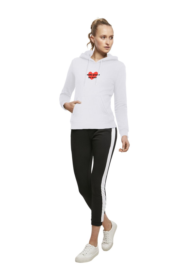 Haut blanc à capuche avec une poche avant et un texte rouge "faire la paix pas la guerre". Associé à un legging noir avec des rayures blanches sur les côtés et des baskets blanches.