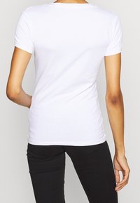 Camiseta blanca de manga corta, hecha de algodón suave con un diseño ajustado. Cuello redondeado y hombros sin costuras; sin gráficos ni patrones.