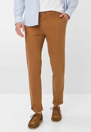 Braune Baumwollhosen mit Slim-Fit, ausgestattet mit einem Knopfverschluss, Seitentaschen und umgeschlagenen Säumen, kombiniert mit braunen Wildlederschuhen.