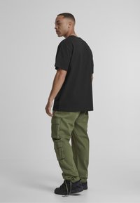 Must päevane must puuvillane t-särk, millele on sobitatud oliivroheline cargo püksid küljetaskutega, täiendab mustad sportjalatsid. Lihtne ja funktsionaalne disain.