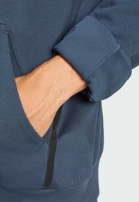 Marineblauer Pullover mit Kängurutasche und elastischen Bündchen, der einen strukturierten Stoff und einen eleganten schwarzen Akzent entlang der Tasche aufweist.