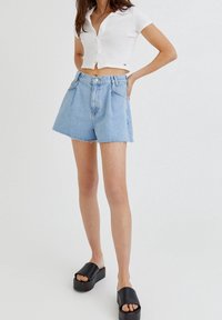 Shorts vaqueros azul claro con cintura alta y dobladillo deshilachado, combinados con una camiseta ajustada blanca de manga corta de canalé y sandalias negras de plataforma.